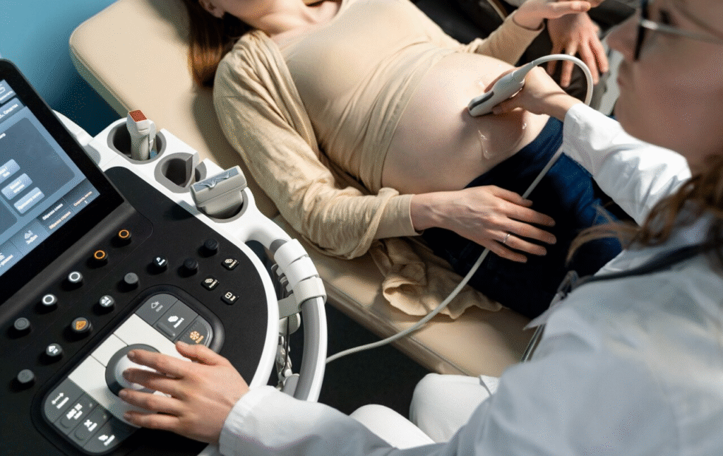 Pregnant woman receiving an abdominal ultrasound, with a medical professional using a transducer to check fetal health on a monitor.