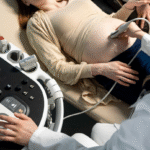 Pregnant woman receiving an abdominal ultrasound, with a medical professional using a transducer to check fetal health on a monitor.