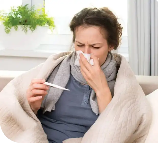 Woman with a blanket holding a thermometer and coughing.