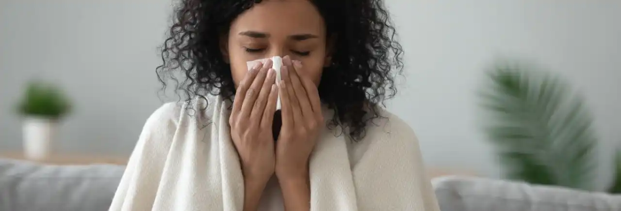 Woman sneezing into a tissue at home.