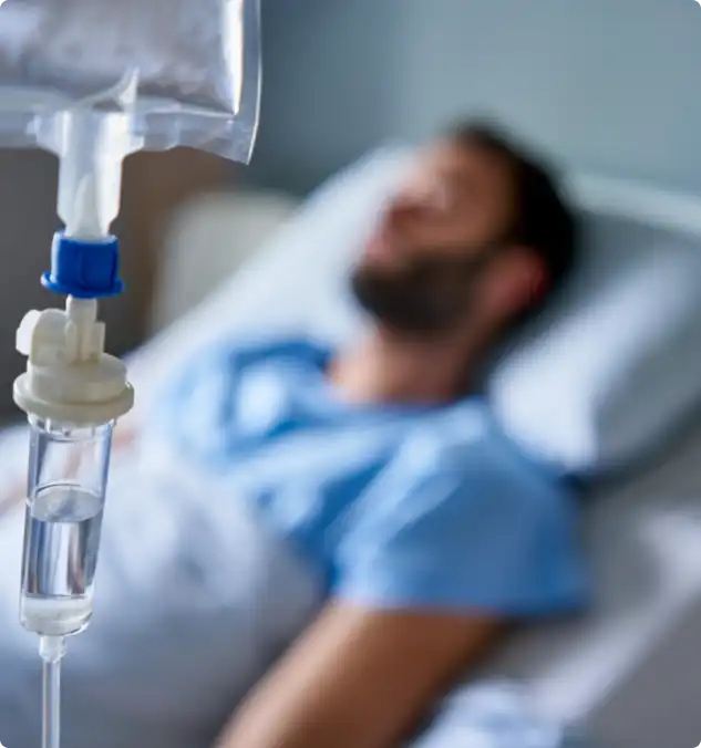 Close-up of an IV drip with a male patient lying in a hospital bed.