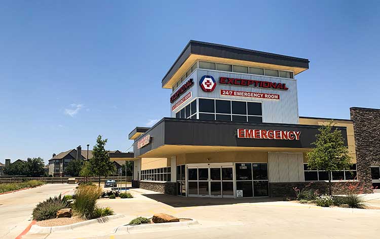 A building labeled "Exceptional Emergency Center" with signage for a 24/7 emergency room. The structure has a modern design with large windows and is surrounded by a landscaped area.