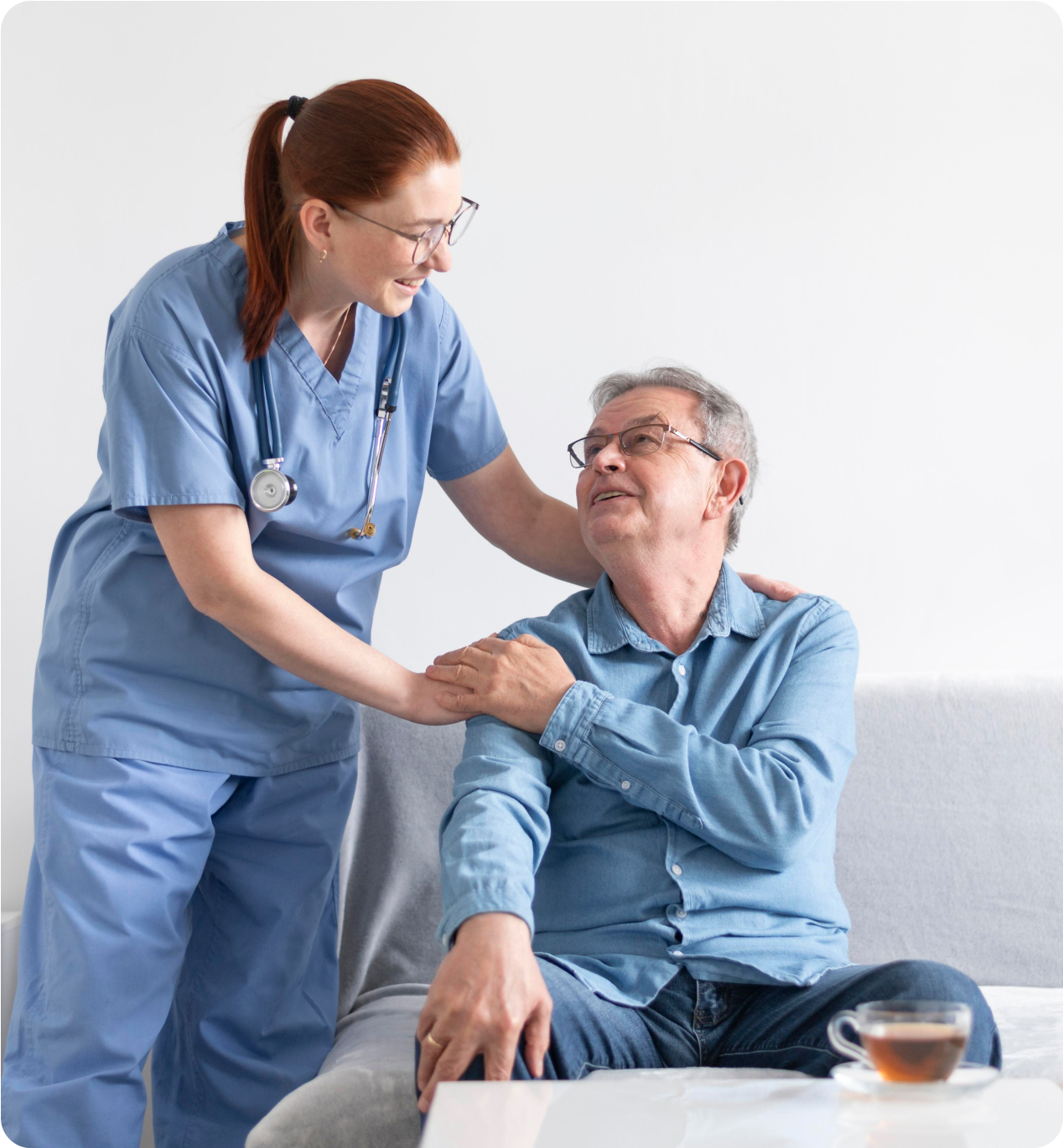 Nurse comforting an older man sitting on a couch during a home care visit.