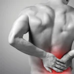 A man is bent slightly forward, visibly suffering from lower right back pain, with his hand on his lower right back.