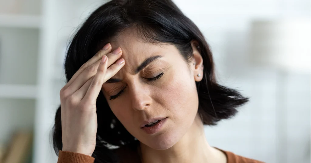 A woman with a pained expression, holding her head, potentially a sign of stroke in women.