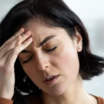 A woman with a pained expression, holding her head, potentially a sign of stroke in women.