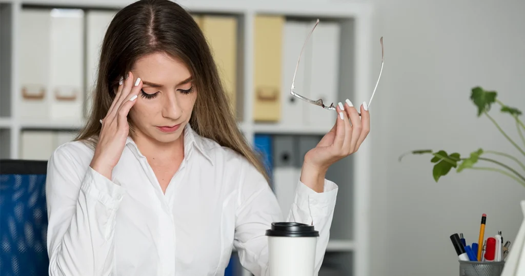 Woman experiencing a tension headache while sitting at a desk, holding her head