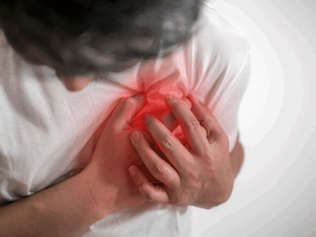 A man clutching his chest, showing signs of burning pain in the chest that may indicate heartburn or a possible medical condition.