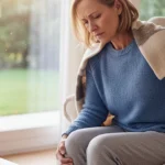 A woman sits in a chair, holding her lower back and knee in pain