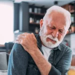Elderly man with white hair experiencing sharp pain in his shoulder