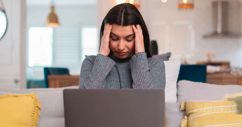 Woman holding her head in frustration while working on a laptop.