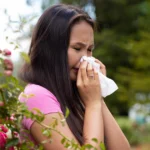 Person with hay fever holding tissue in garden.