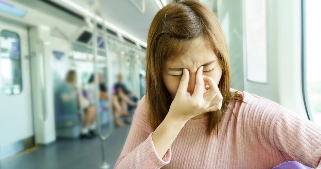 Woman experiencing sinus infection symptoms on subway.