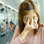 Woman experiencing sinus infection symptoms on subway.