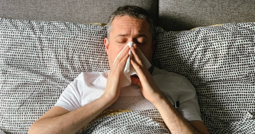 Man in bed holding tissue, experiencing nasal congestion.