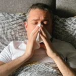 Man in bed holding tissue, experiencing nasal congestion.