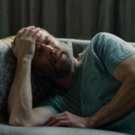 A man lies on a couch, clutching his head in pain. Some use magnesium to lower blood pressure and manage migraines.