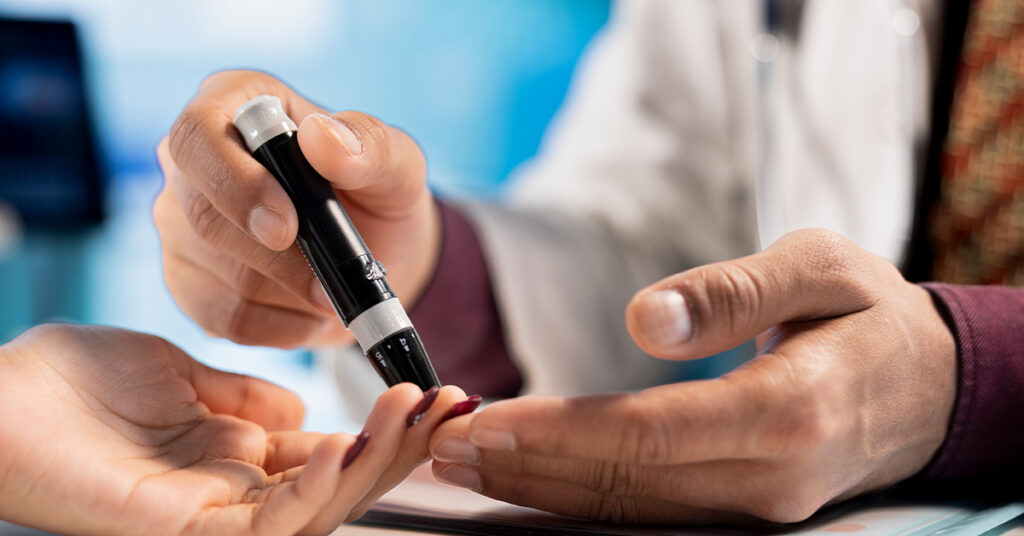 A healthcare professional assists a patient with a blood glucose finger-prick test using a lancing device.