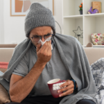 Sick man with flu symptoms resting on a couch.