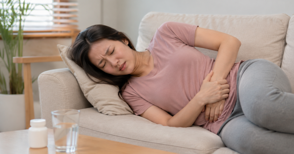 Woman lying on a couch holding her lower left abdomen in pain.