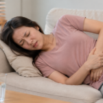 Woman lying on a couch holding her lower left abdomen in pain.