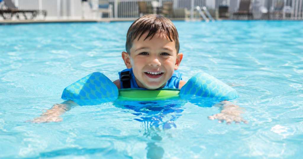 Young boy swimming safely with floaties in a pool.