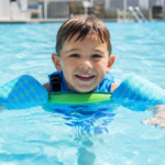Young boy swimming safely with floaties in a pool.