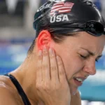 Female swimmer holding her red, painful ear beside a swimming pool.