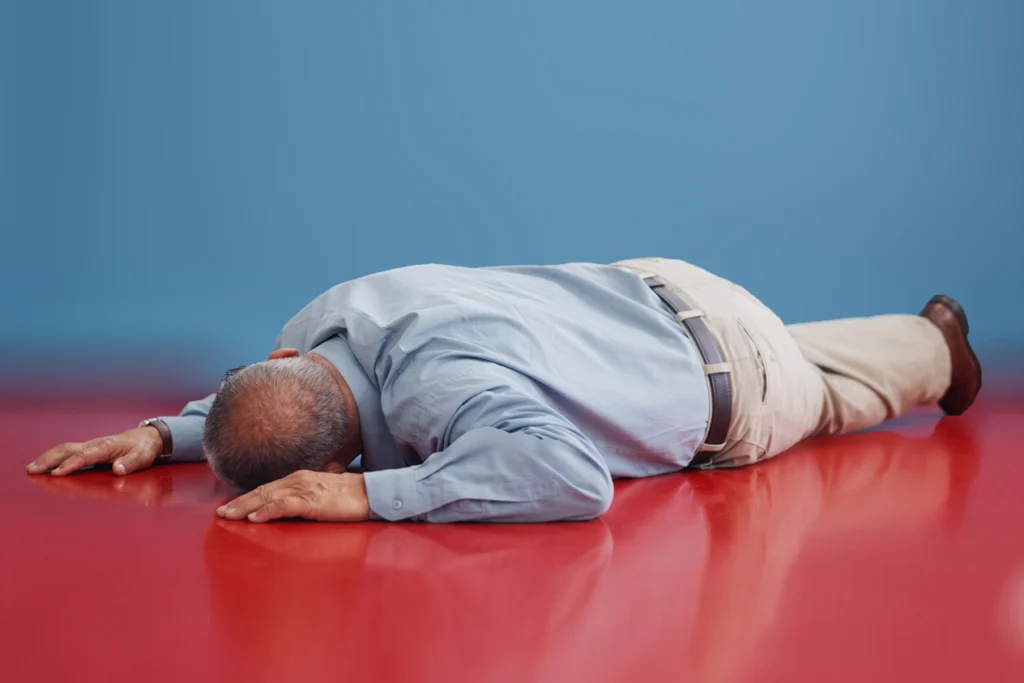 A person unconsciously lying face-down on a red floor and blue background.