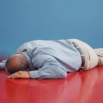 A person unconsciously lying face-down on a red floor and blue background.