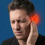 A man grimacing in pain and touching his ear, which is highlighted with a red glow to indicate discomfort or injury.