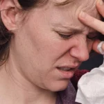 A woman holding her head and a tissue in pain.