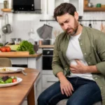 Adult experiencing stomach discomfort in a modern kitchen (Food Poisoning).