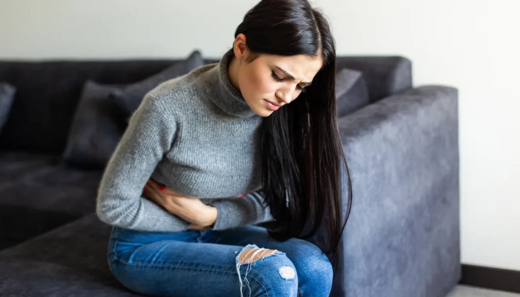 Woman sitting on a sofa clutching her stomach in pain.