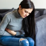 Woman sitting on a sofa clutching her stomach in pain.