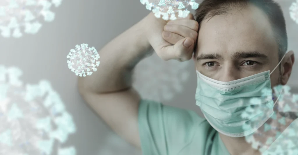 A man in a green shirt is holding his head, appearing distressed, possibly due to illness or stress related to a virus.