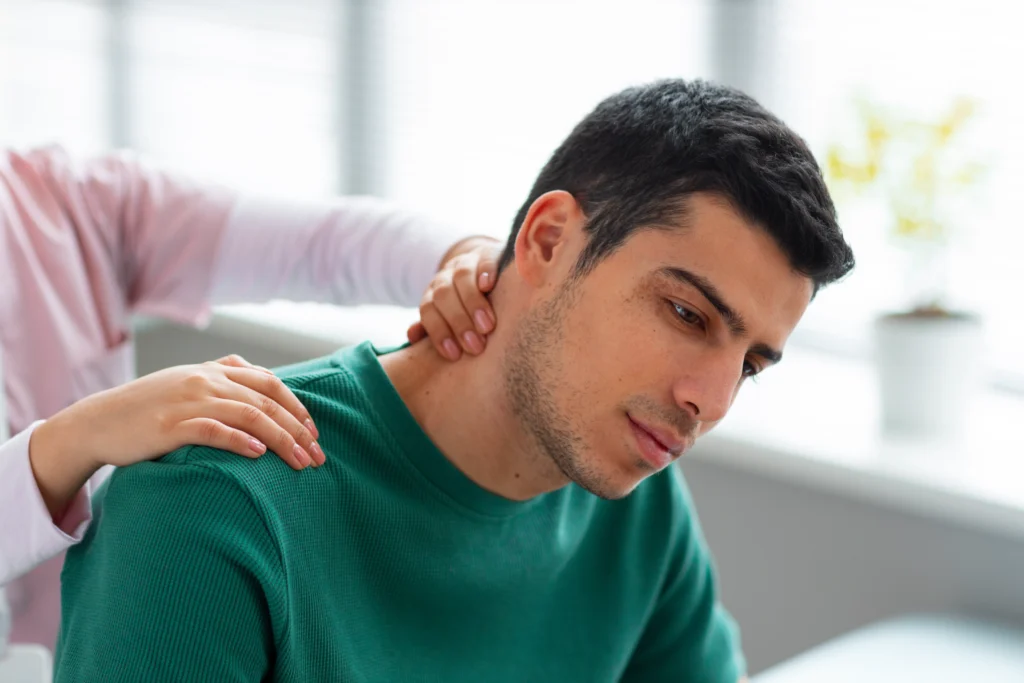 Healthcare provider or physical therapist examining a young man's neck and shoulder.