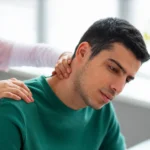 Healthcare provider or physical therapist examining a young man's neck and shoulder.